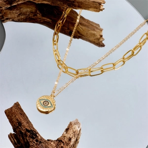 Gold double-layer evil eye pendant necklace on mirror surface with rustic wood accents
