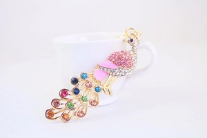 Detailed close-up of colorful rhinestone peacock keychain with pink enamel on gold metal