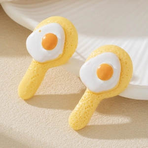 Orecchini a perno a forma di uovo fritto in resina su un piatto di ceramica bianca
