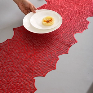 Detail of red hollow spider web table runner with metallic gold accents for Halloween decor