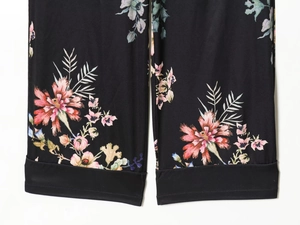 Detail view of black floral pants featuring pink and purple flower prints and hem stitching