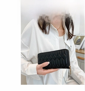 Detail view of black quilted long wallet with golden zipper held by a female model