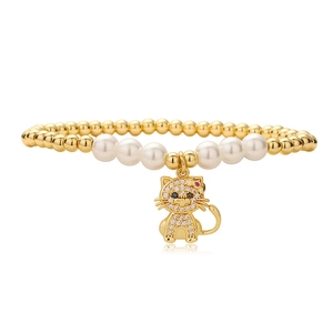 Dettaglio bracciale con perle, sfere dorate e un ciondolo a forma di gatto scintillante