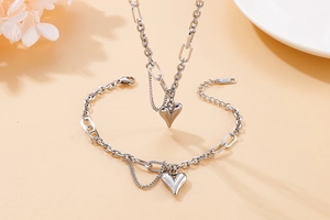 Detail of silver stainless steel heart pendant necklace and bracelet set on beige background