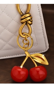 Detail of red resin cherry pendant with golden leaf on a white quilted handbag