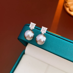 Close-up of silver-gray pearl earrings with geometric zircon inlay on jewelry box