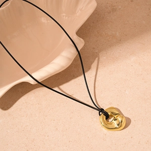 Macro detail of polished irregular gold pendant on smooth black adjustable cord