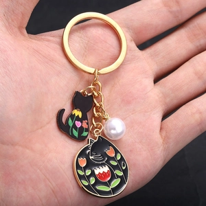Dettaglio portachiavi dorato con ciondoli gatto in smalto nero e accessorio con perla