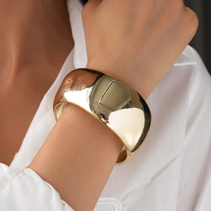 Close-up of polished gold-finished wide bangle showing mirror texture and geometric arc