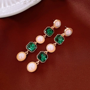 Detail of vintage gold earrings with emerald green stones and pearls on dark background