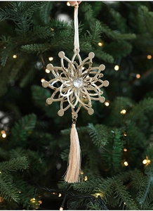 Close-up of champagne gold snowflake ornament with gem and silk tassel on a Christmas tree