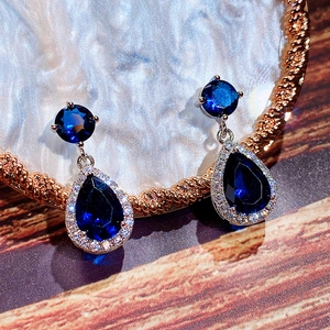 Detailed close-up of teardrop royal blue zircon earrings with silver diamond setting