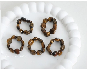 Detailed top view of five elastic tiger eye beaded rings on a white bubbly tray