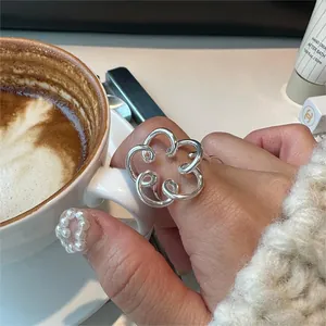 Close-up of a minimalist hollow floral silver ring worn on a finger holding a coffee cup