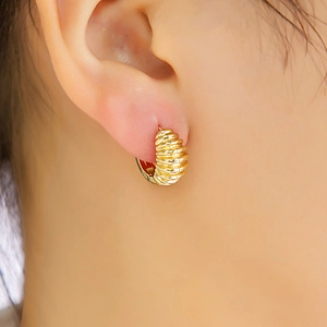 Gros plan d'une boucle d'oreille dorée texturée portée par un mannequin avec détails