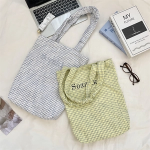 Detail view of plaid canvas tote bags in grey and yellow patterns on a white bed