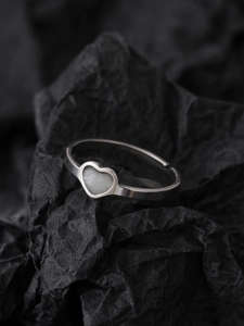 Detailed view of an open silver ring with a white heart-shaped gemstone on black paper