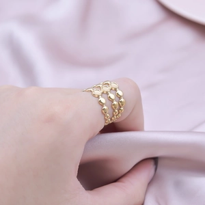 Close-up of a three-layered gold beaded ring worn on index finger over silk fabric