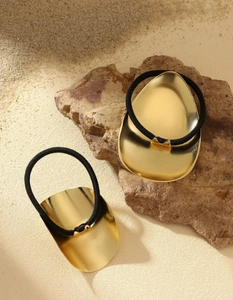 Close-up of gold oval metal hair ties with black elastic bands on a stone background