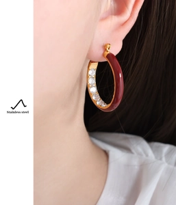 Close-up of gold stainless steel hoop earrings with burgundy enamel and clear crystals