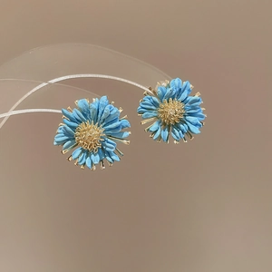 Detailed view of blue daisy earrings with textured petals and golden sunburst center