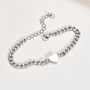 Detail view of a polished silver heart pendant on a chunky Cuban chain bracelet