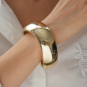 Close-up of wide polished gold metal cuff bracelet worn on a wrist showing high-gloss shine