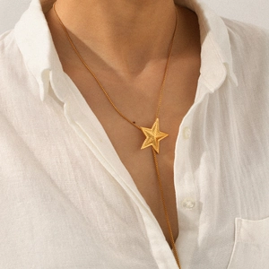 Long stainless steel necklace with textured gold star pendant worn by model on white shirt