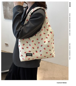 Detail of strawberry print corduroy tote bag worn by model with fashion label
