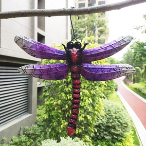 Detailed close-up of a purple and red gradient metal dragonfly wall decor hanging outdoors