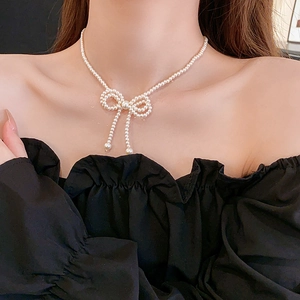 Detail view of a bow-knot pearl necklace with delicate tassel worn by a model