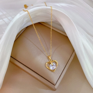 Close-up of golden heart pendant with zircon on silk fabric in beige jewelry box