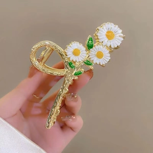 Detail of floral hair claw clip featuring white daisies and gold metal weaving texture