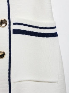Macro detail of white knit vest featuring navy stripes and luxury gold metal buttons