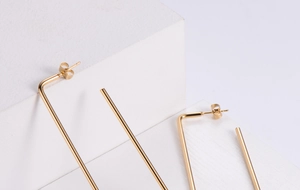 Close-up of minimalist gold-plated rectangular hoop earrings on a white stone base