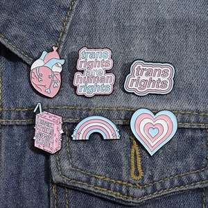 Detail of six trans rights enamel pins on blue denim fabric with rainbow heart and milk box