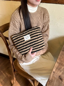 Winter plush makeup bag with brown stripes and colorful label held by a model