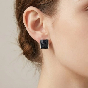 Detailed close-up of a square faceted black stone stud earring with silver metal base on ear