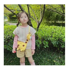 Detail of yellow knitted giraffe crossbody bag worn by a child in an outdoor setting