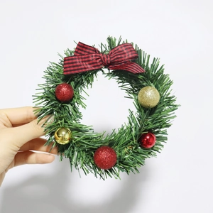Mini Christmas wreath with red plaid bow and glitter balls held against a plain background