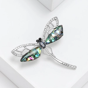 Elegant dragonfly brooch with abalone shell wings and sparkling crystals on white base