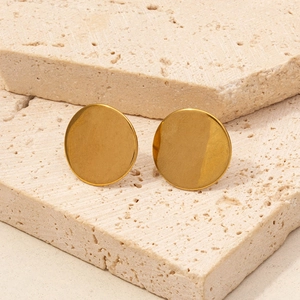 Macro view of minimalist 304 stainless steel gold round stud earrings on travertine stone