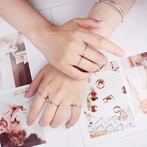 Minimalist silver stackable rings and thin tube bracelet styled on a hand over a magazine