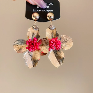 Close-up of golden flower earrings with red centers and textured petals on a black tag