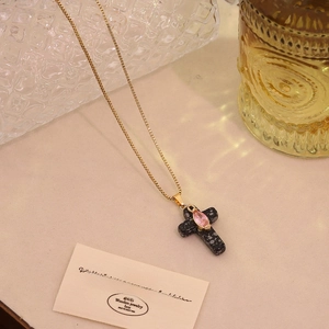 Close-up of a gold cross necklace with black stone and pink marquise gem detail