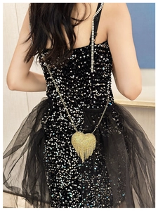 Close-up of a heart-shaped gold evening bag with rhinestones and fringe on a sequin dress