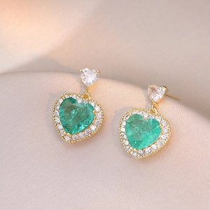 Detail of heart-shaped gold earrings with emerald green stones and zircon accents
