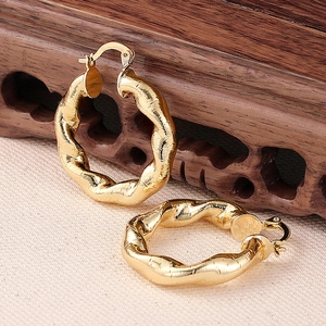 Makroaufnahme goldener Creolen mit gedrehtem Design und strukturierter Spirale auf Holz