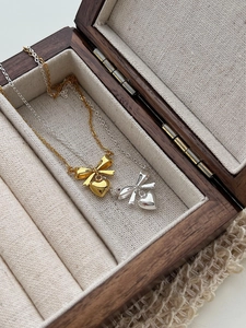 Detail of gold and silver bow heart necklaces presented in a premium wooden jewelry box