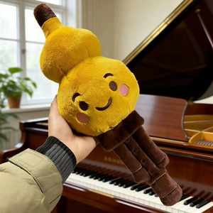 Cute golden gourd plush toy with embroidered smiling face being held against a piano